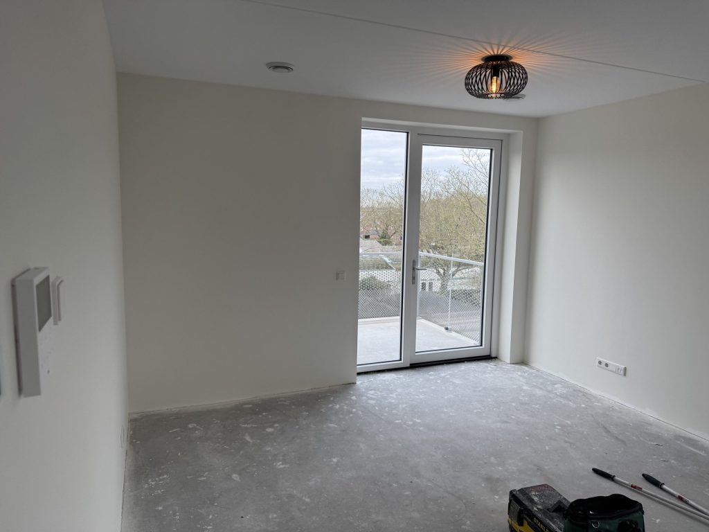 Lege kamer in een nieuw appartement met balkondeuren en een kale betonvloer, kort na de oplevering