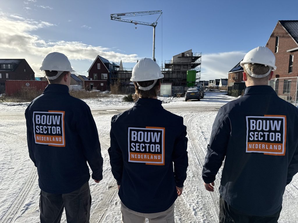 Drie vakmensen van Bouwsector Nederland met witte helm op een besneeuwde straat met nieuwbouw in aanbouw